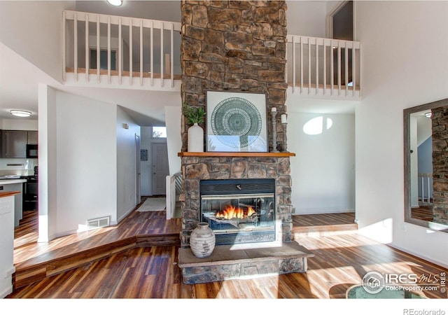 living room featuring hardwood / wood-style flooring, a towering ceiling, and a stone fireplace