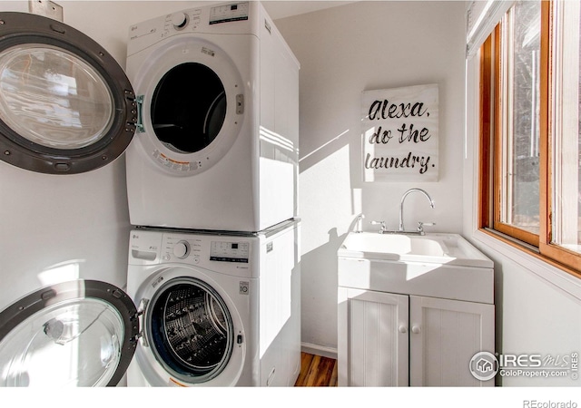 washroom with cabinets, stacked washer / dryer, and sink