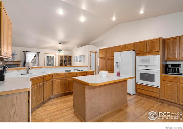 kitchen featuring vaulted ceiling, sink, a center island, kitchen peninsula, and white appliances