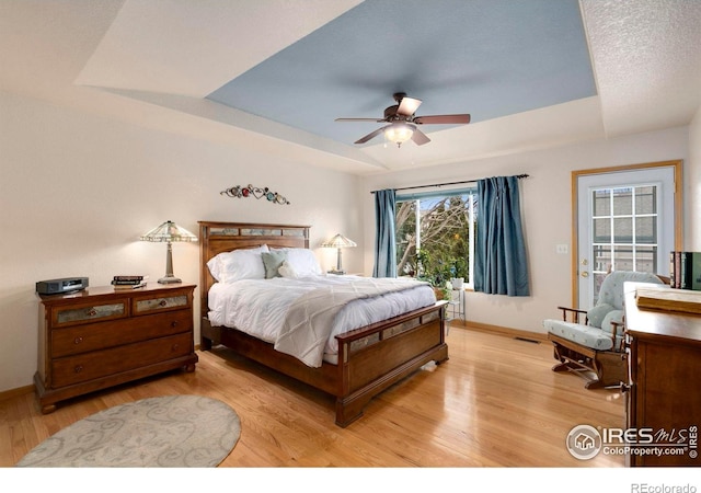 bedroom with a raised ceiling, ceiling fan, access to exterior, and light wood-type flooring