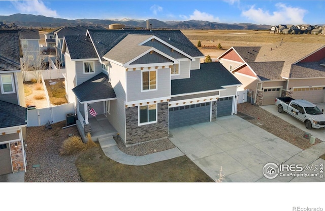 view of front of house with driveway, stone siding, fence, cooling unit, and a mountain view