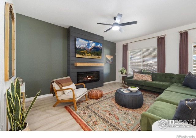 living room featuring a large fireplace, baseboards, a ceiling fan, and wood finished floors