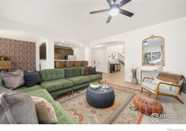 living room featuring arched walkways, ceiling fan, an accent wall, wood finished floors, and wallpapered walls