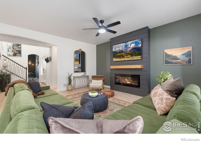 living area featuring arched walkways, a fireplace, wood finished floors, baseboards, and stairs