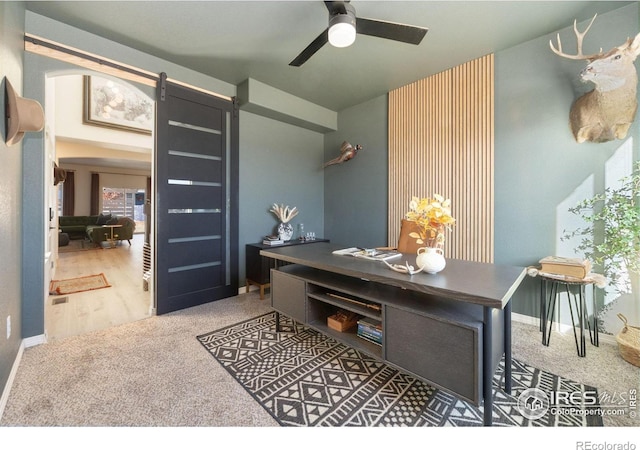 home office featuring a ceiling fan, carpet floors, baseboards, and a barn door