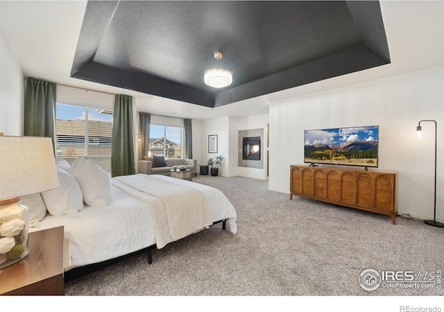 bedroom featuring carpet floors, a raised ceiling, a fireplace, and baseboards