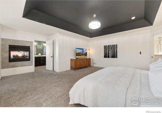 carpeted bedroom featuring baseboards, a raised ceiling, connected bathroom, and a multi sided fireplace