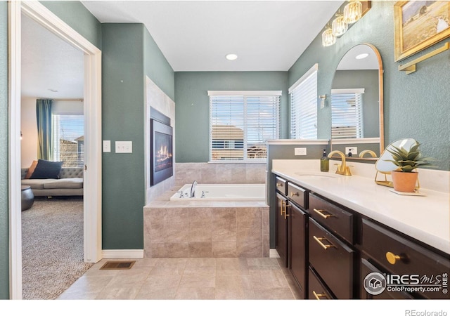 full bathroom featuring tile patterned flooring, a garden tub, visible vents, vanity, and a glass covered fireplace