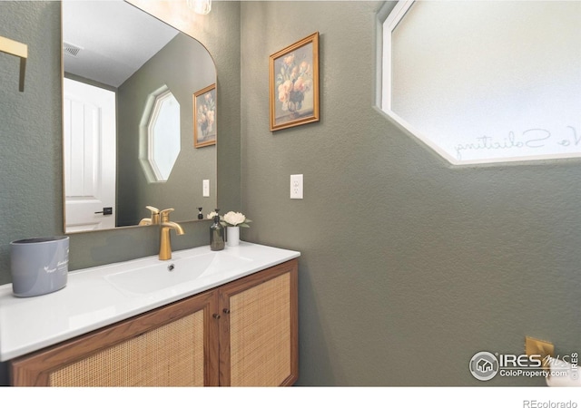 bathroom with a textured wall, vanity, and visible vents