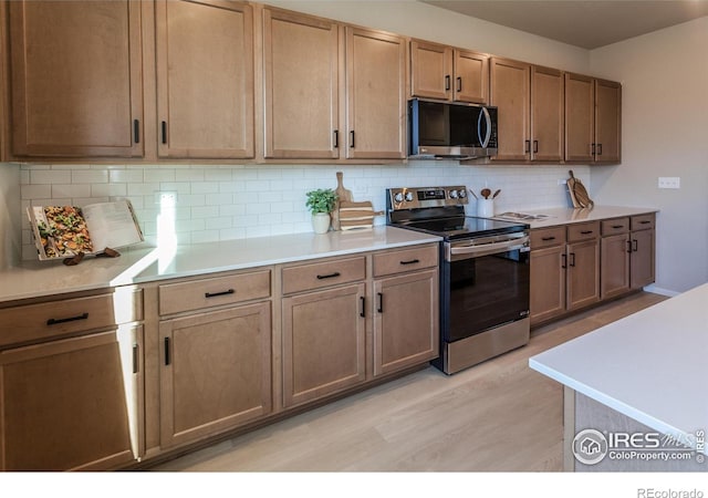 kitchen featuring stainless steel appliances, backsplash, and light wood-type flooring