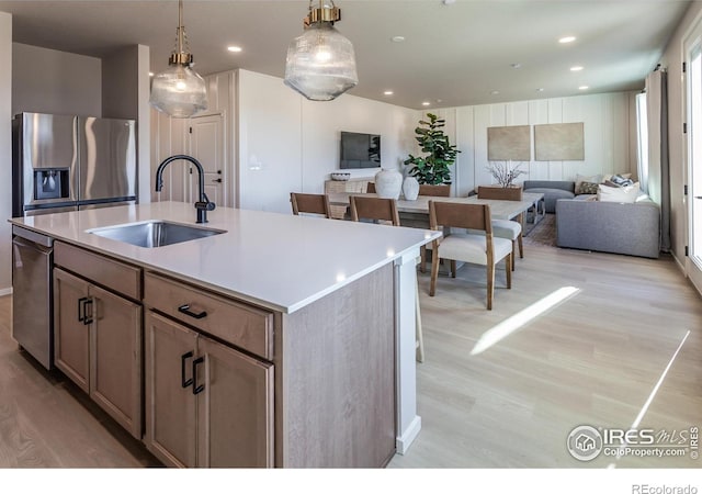 kitchen with sink, light hardwood / wood-style flooring, appliances with stainless steel finishes, a kitchen island with sink, and decorative light fixtures