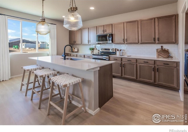 kitchen featuring sink, decorative light fixtures, stainless steel appliances, a kitchen island with sink, and backsplash