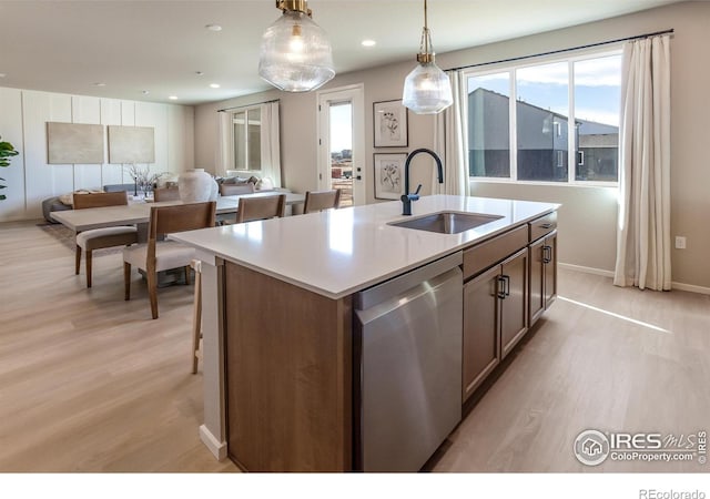 kitchen featuring pendant lighting, an island with sink, sink, stainless steel dishwasher, and light wood-type flooring