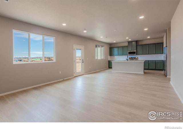 kitchen featuring light wood finished floors, baseboards, open floor plan, recessed lighting, and appliances with stainless steel finishes