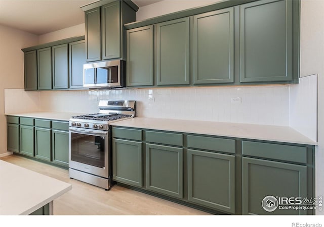 kitchen with green cabinetry, backsplash, appliances with stainless steel finishes, and light countertops