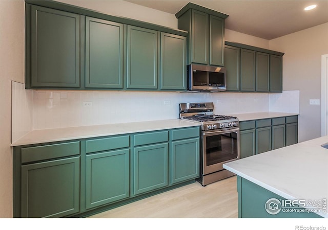 kitchen with backsplash, light countertops, light wood-style floors, stainless steel appliances, and green cabinetry