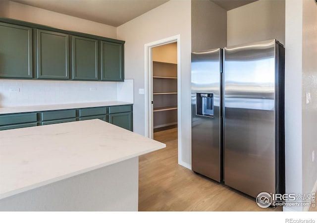 kitchen with light wood-style flooring, tasteful backsplash, green cabinets, stainless steel fridge with ice dispenser, and light countertops