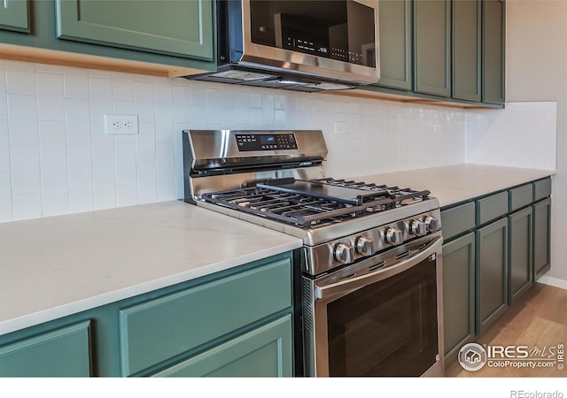 kitchen featuring light wood finished floors, green cabinetry, stainless steel appliances, light countertops, and tasteful backsplash