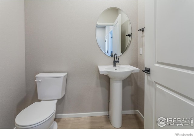 half bathroom featuring toilet, baseboards, and wood finished floors