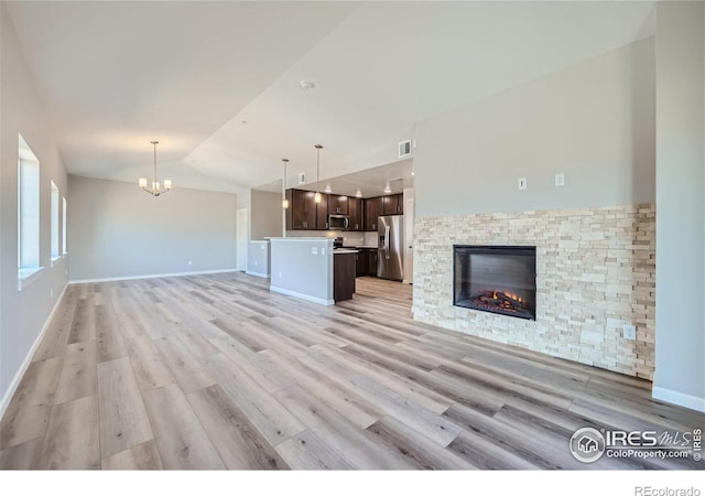 unfurnished living room with a stone fireplace, a chandelier, high vaulted ceiling, and light wood-type flooring