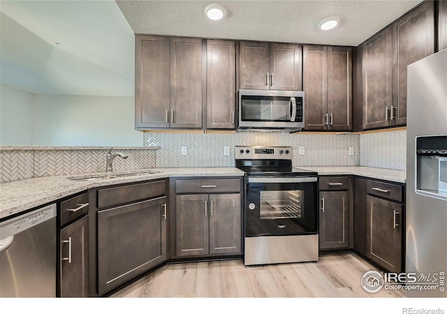 kitchen with light stone counters, appliances with stainless steel finishes, sink, and dark brown cabinets