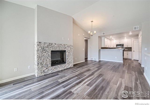 unfurnished living room featuring hardwood / wood-style flooring, vaulted ceiling, and an inviting chandelier