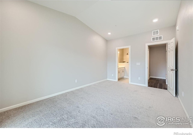 unfurnished bedroom with vaulted ceiling, connected bathroom, and light colored carpet