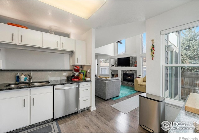 kitchen featuring sink, white cabinets, dark stone counters, stainless steel dishwasher, and light wood-type flooring