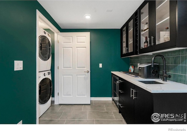 laundry area featuring light tile patterned flooring, stacked washing maching and dryer, and sink