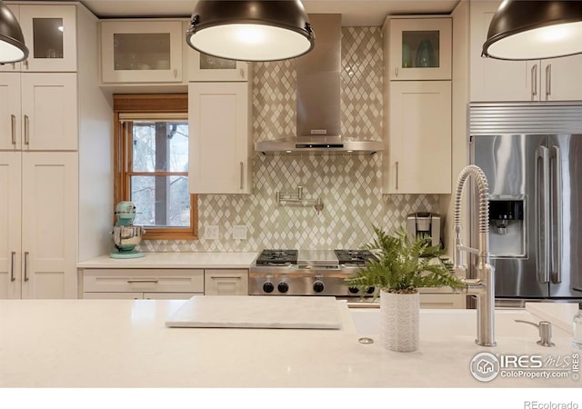 kitchen with stainless steel fridge, glass insert cabinets, range, light countertops, and wall chimney exhaust hood