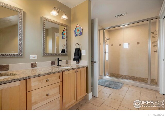 bathroom with a shower stall, double vanity, a sink, and tile patterned flooring