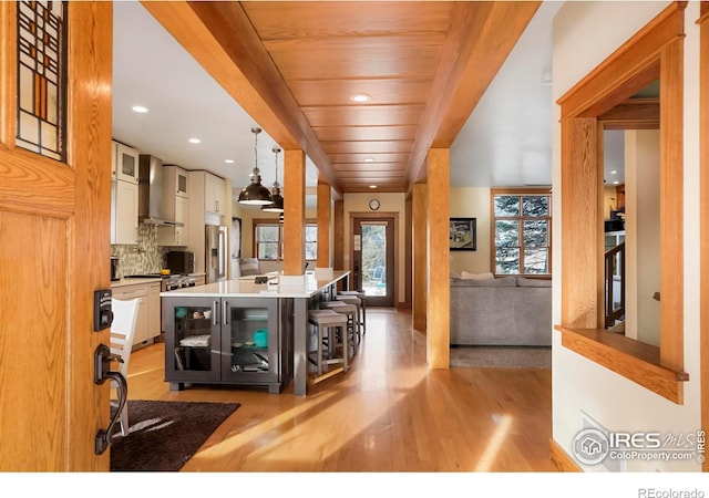 kitchen with a center island, hanging light fixtures, a kitchen bar, wall chimney exhaust hood, and glass insert cabinets