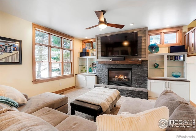 living room with light colored carpet, recessed lighting, baseboards, a stone fireplace, and ceiling fan