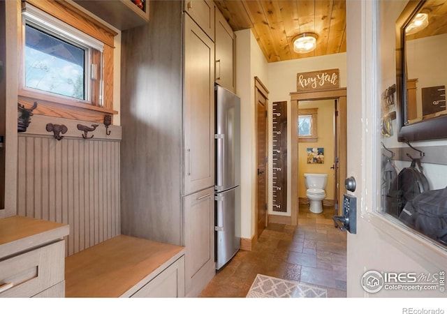 interior space with freestanding refrigerator, baseboards, wooden ceiling, stone tile floors, and light countertops