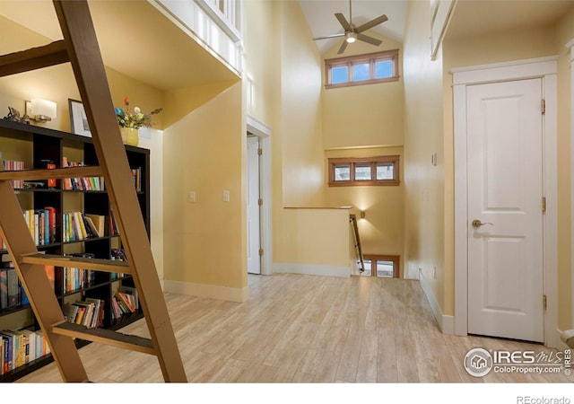 hallway with light wood-style flooring, baseboards, a towering ceiling, and an upstairs landing