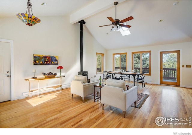 living room featuring high vaulted ceiling, a wood stove, beamed ceiling, ceiling fan, and light hardwood / wood-style floors