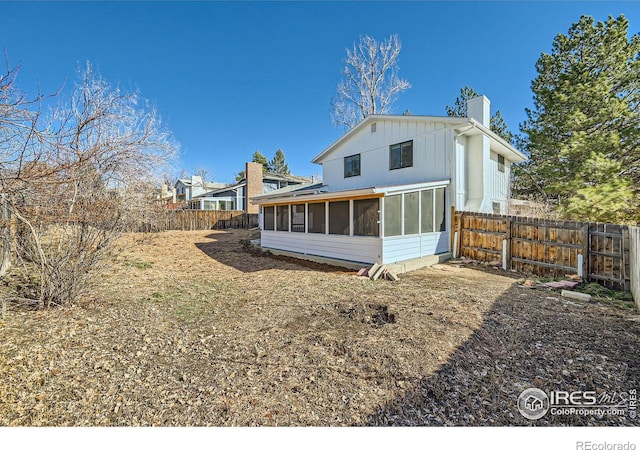 rear view of house with fence, board and batten siding, a chimney, and a sunroom