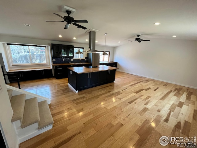 kitchen featuring a center island, dark cabinets, light wood-style flooring, island range hood, and a sink