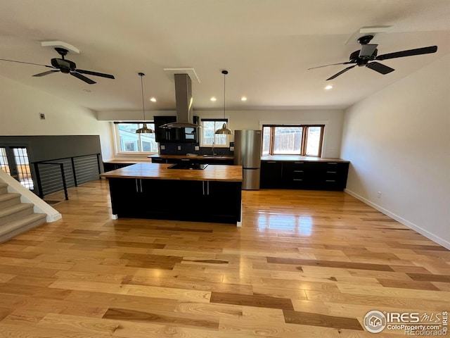 kitchen featuring dark cabinets, island exhaust hood, freestanding refrigerator, light wood-type flooring, and a center island