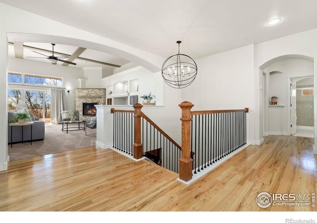 stairs featuring ceiling fan, wood-type flooring, a stone fireplace, and beam ceiling