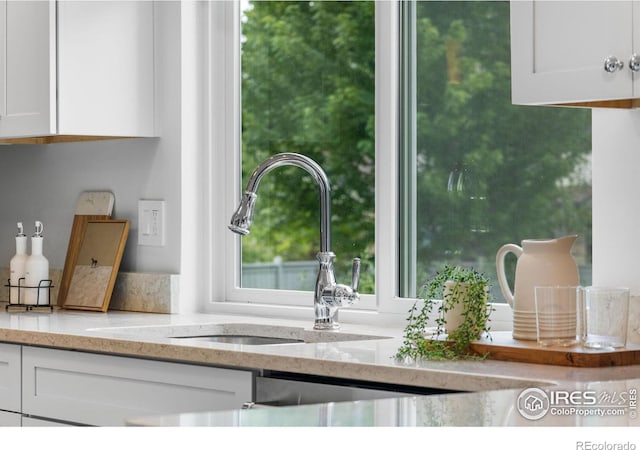 details featuring sink, white cabinets, and light stone counters