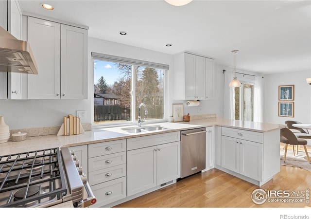 kitchen featuring sink, appliances with stainless steel finishes, kitchen peninsula, pendant lighting, and wall chimney range hood