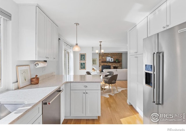 kitchen with pendant lighting, white cabinetry, stainless steel appliances, kitchen peninsula, and light wood-type flooring