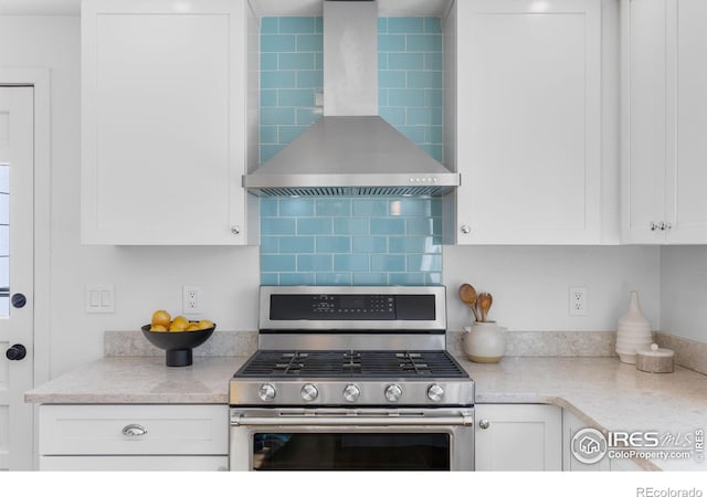 kitchen with stainless steel gas stove, wall chimney range hood, decorative backsplash, and white cabinets