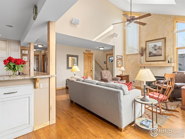 living room with ceiling fan, a fireplace, high vaulted ceiling, and light hardwood / wood-style flooring