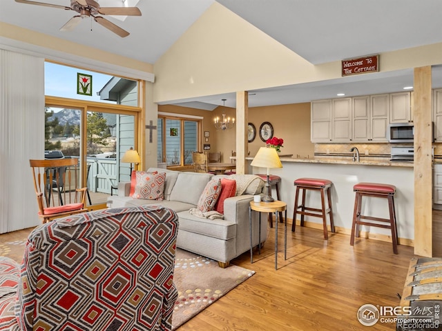 living room with ceiling fan with notable chandelier, high vaulted ceiling, sink, and light hardwood / wood-style floors