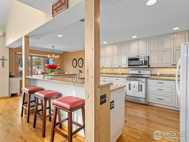 kitchen featuring decorative light fixtures, backsplash, a kitchen bar, stainless steel appliances, and light stone countertops