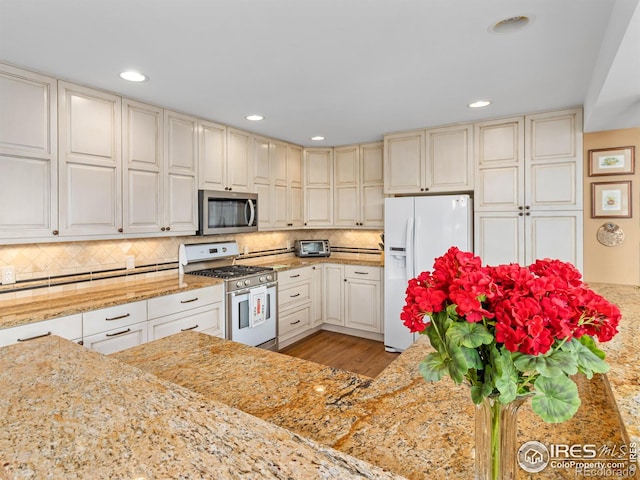 kitchen featuring stainless steel appliances, light stone countertops, light hardwood / wood-style flooring, and backsplash