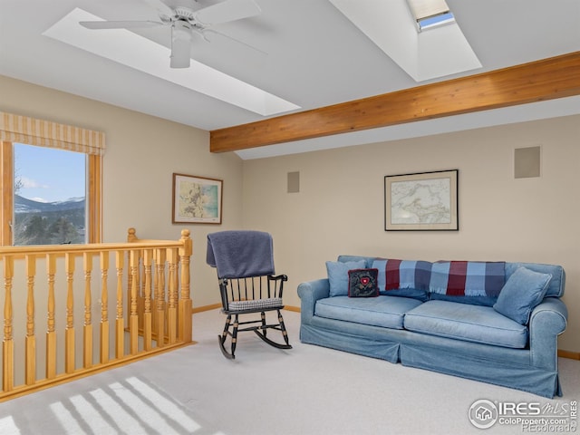 carpeted living room featuring ceiling fan, a skylight, and beamed ceiling