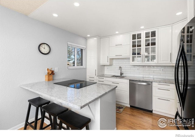 kitchen with white cabinetry, a kitchen bar, kitchen peninsula, and black appliances